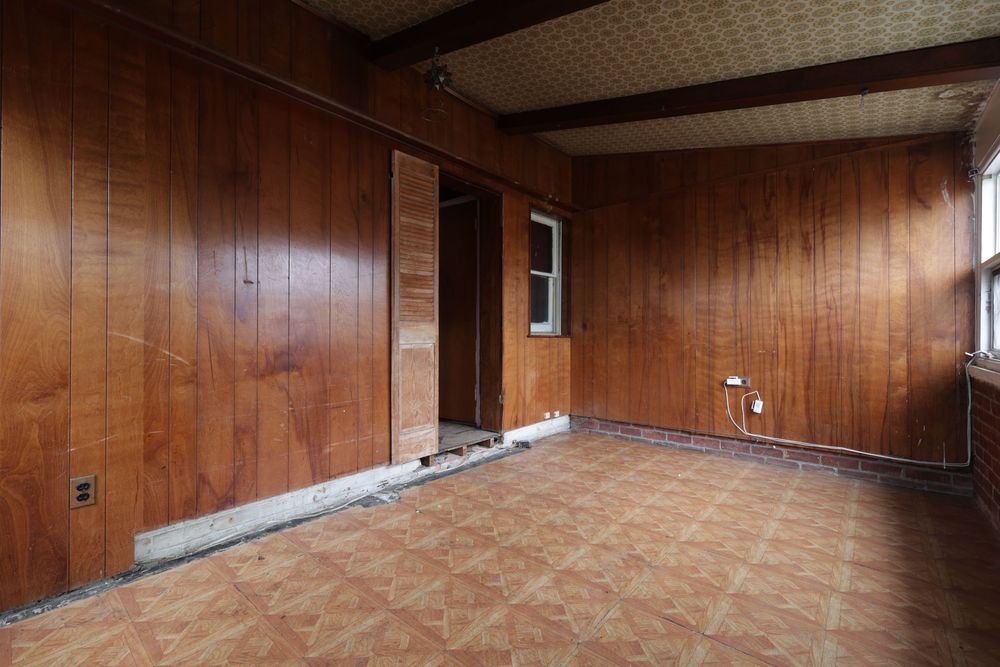 Empty room with wood-paneled walls, tile flooring, and a sliding door in a vacant property.