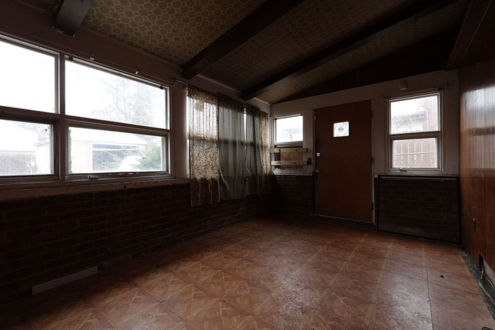 Dimly lit empty room with brick wall, wood beam ceiling, large windows, and brown door in a vintage interior.