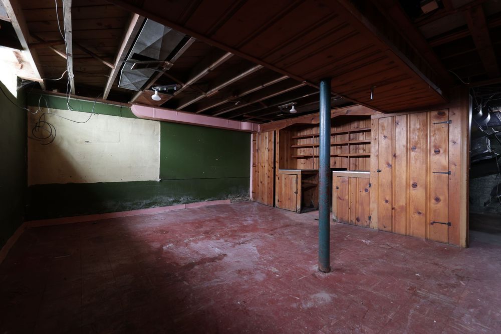 Unfinished basement with exposed ceiling joists, wood-paneled walls, built-in shelving, green accent wall, and red concrete floors.