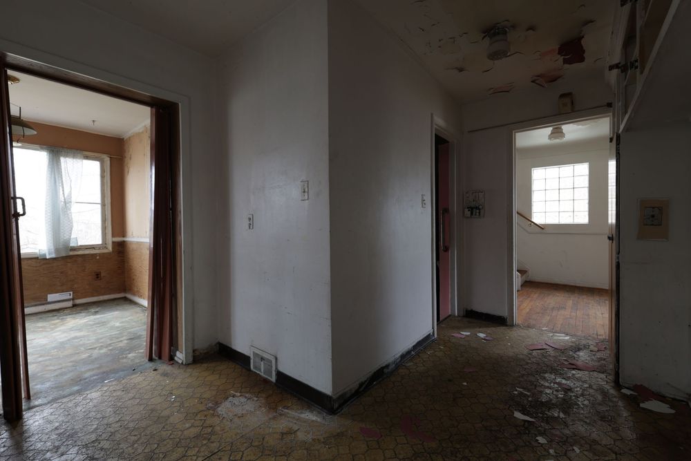 Abandoned building interior with deteriorating walls, damaged floors, and multiple doorways leading to empty rooms.