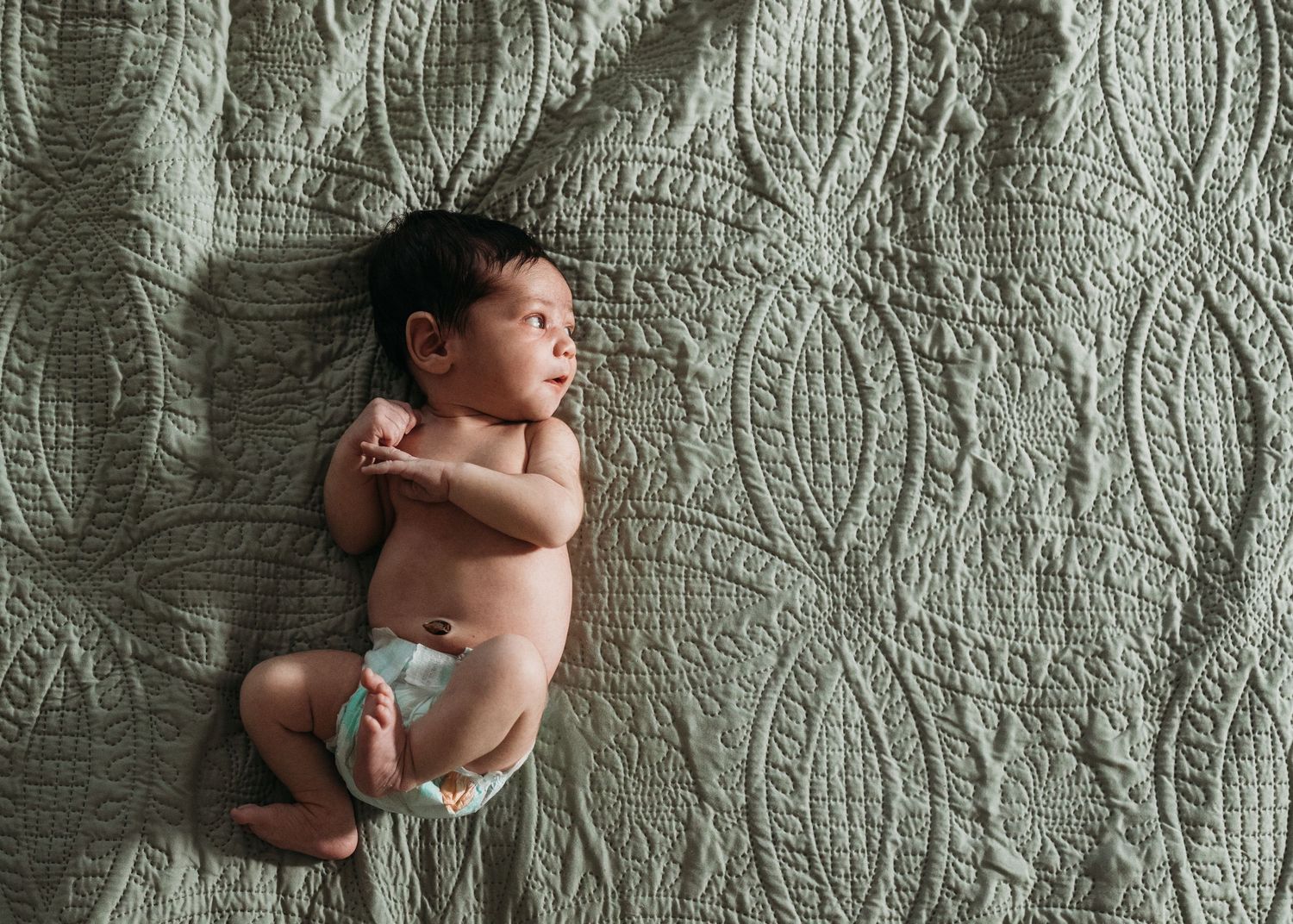 Newborn baby in diaper lying on green textured quilt blanket, peaceful infant portrait photography.