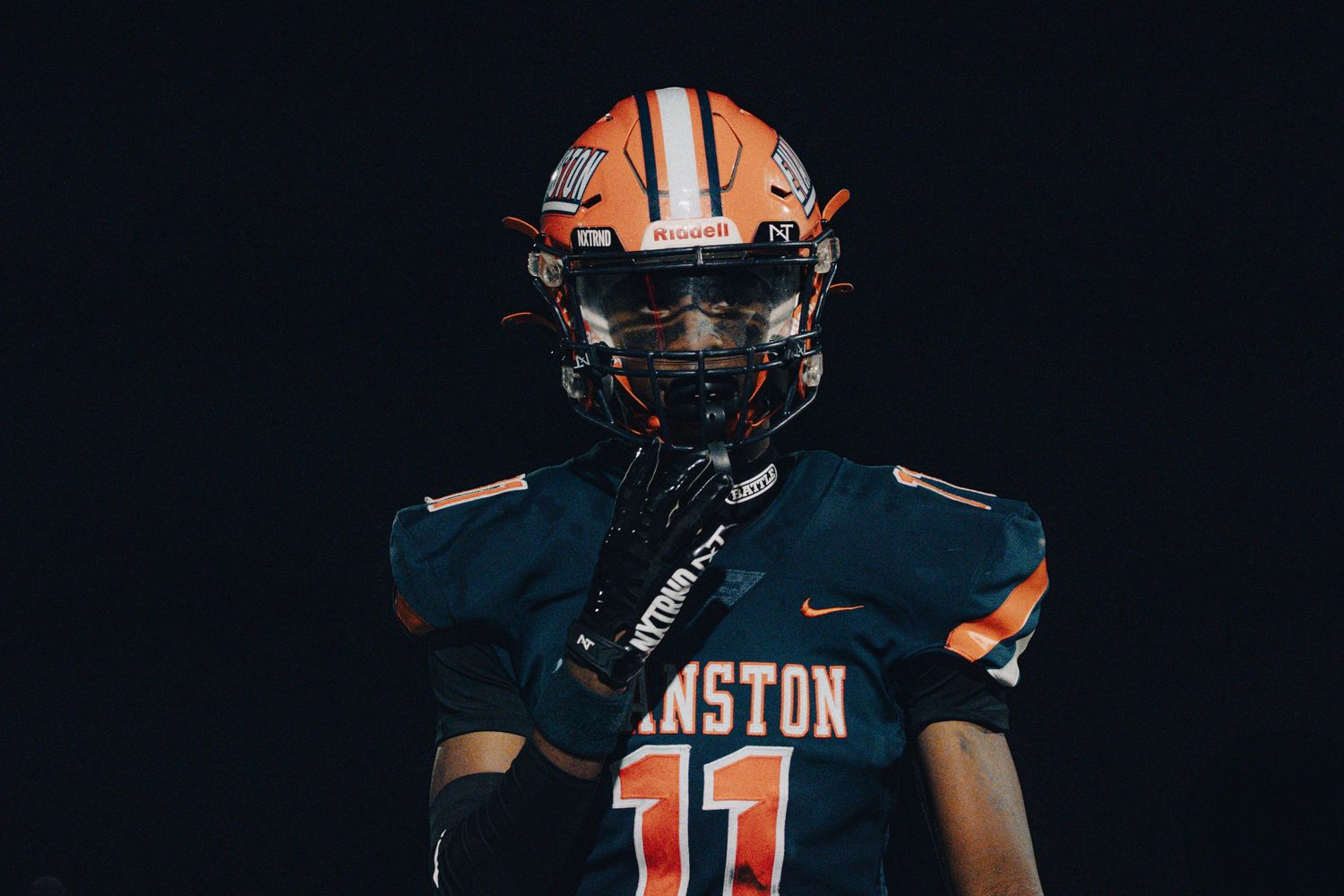 Football player wearing navy and orange uniform with number 11 jersey and orange helmet against dark background.
