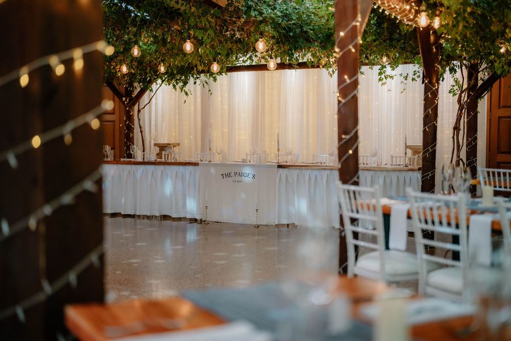 Rustic wooden barn interior illuminated with string lights and white chairs set up for an indoor event.