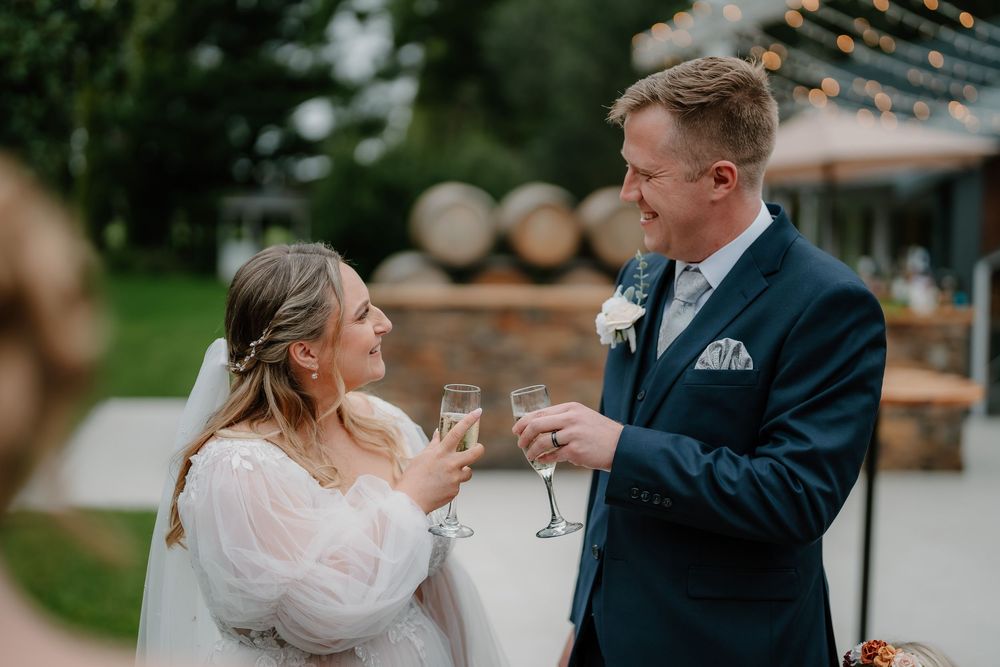 A couple shares a toast with champagne glasses during their outdoor wedding celebration.