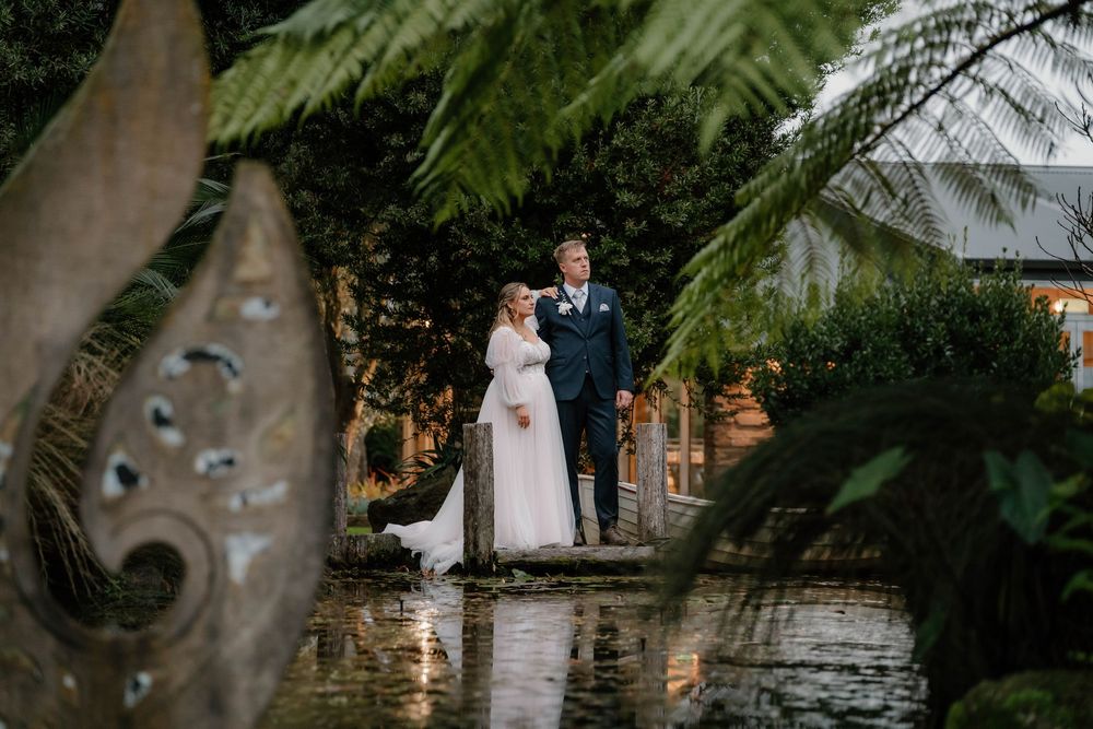 A couple shares a romantic moment on a wet walkway surrounded by tropical ferns and garden decor.
