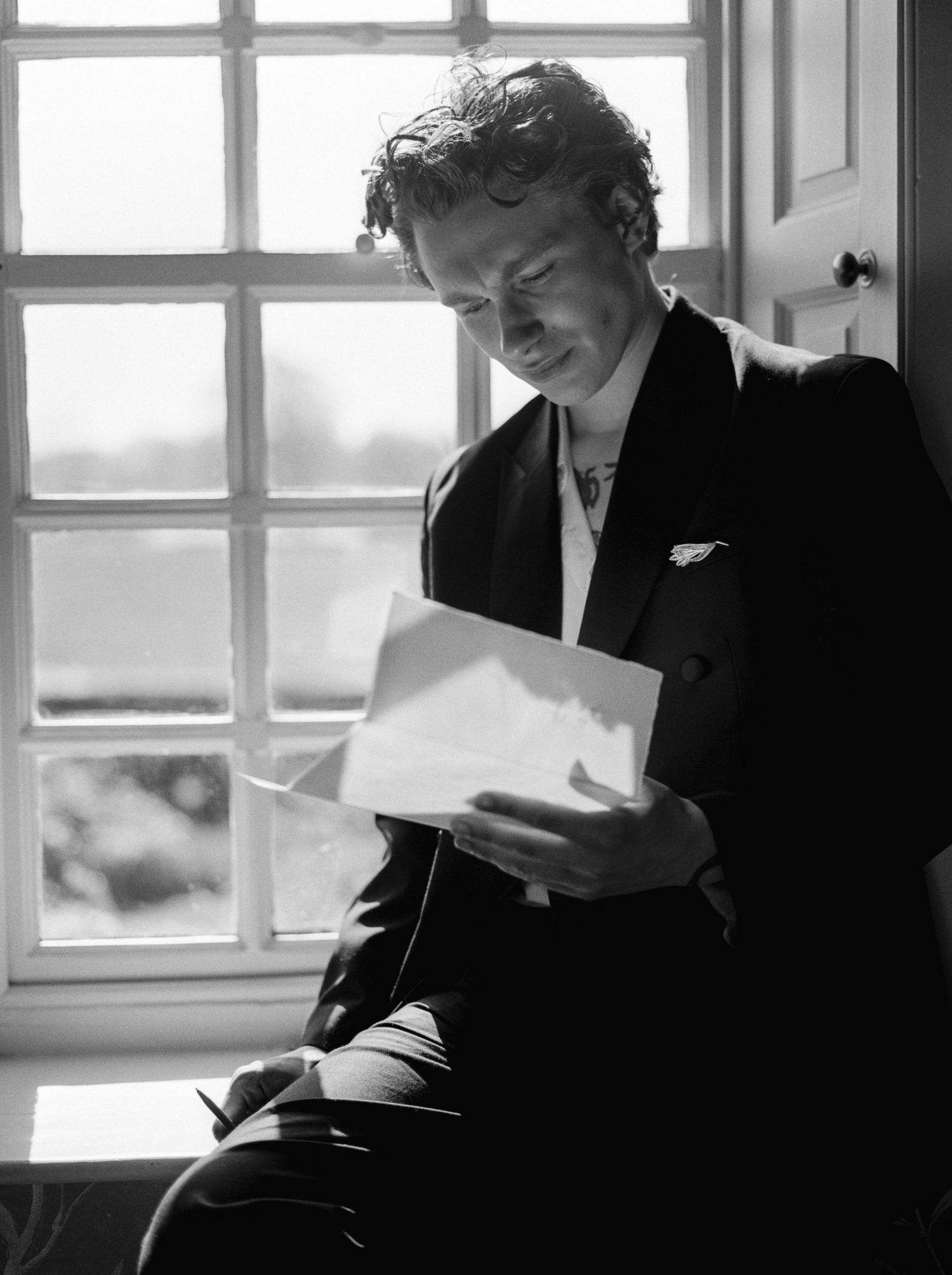 Black and white photo of a man in a suit reading a letter by a bright window, elegant and contemplative mood.