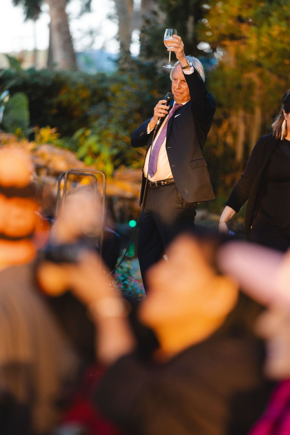 Man in black suit raises champagne glass during outdoor evening toast at elegant event.