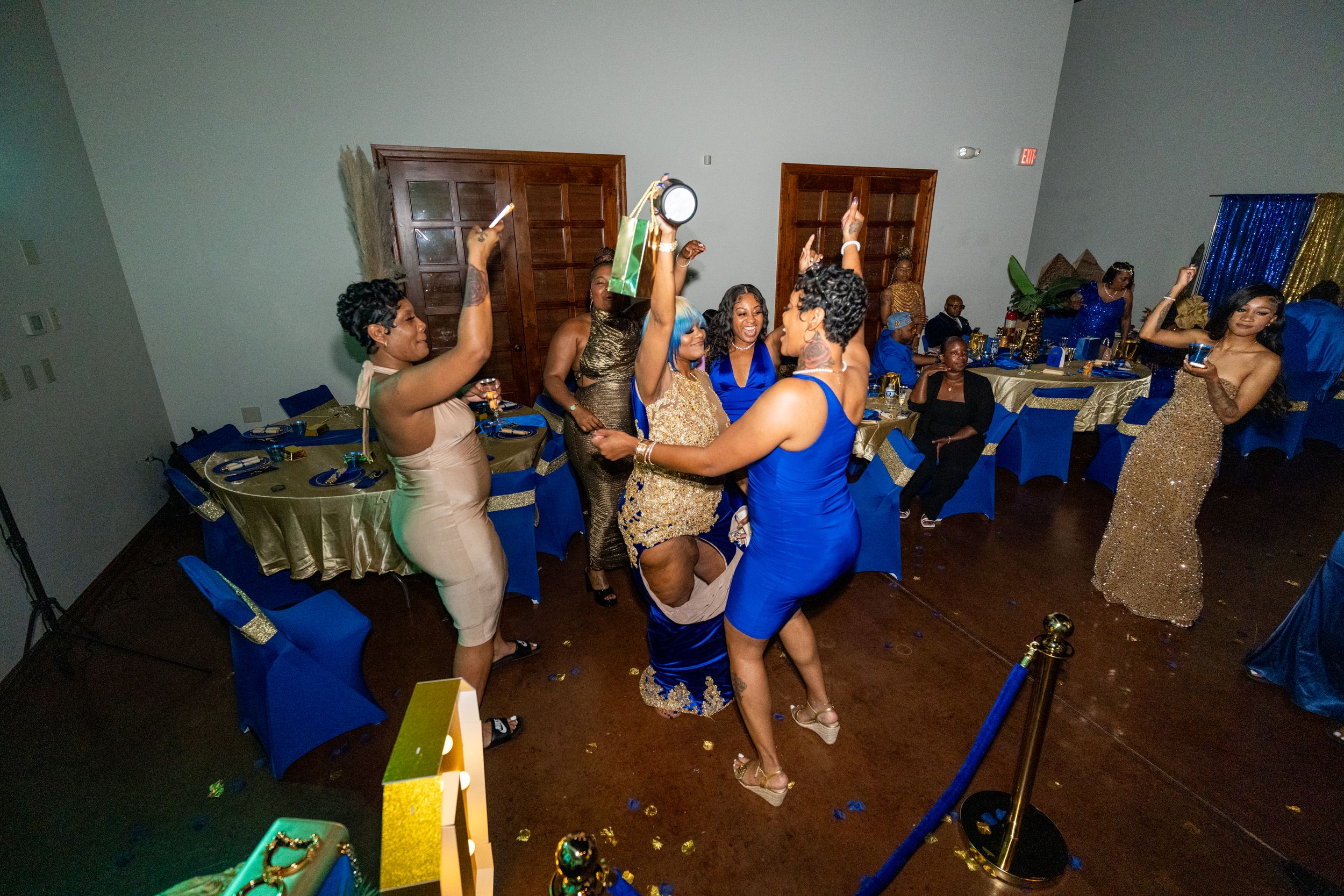 Women in blue dresses dancing and celebrating at an elegant banquet hall event with blue table decorations.