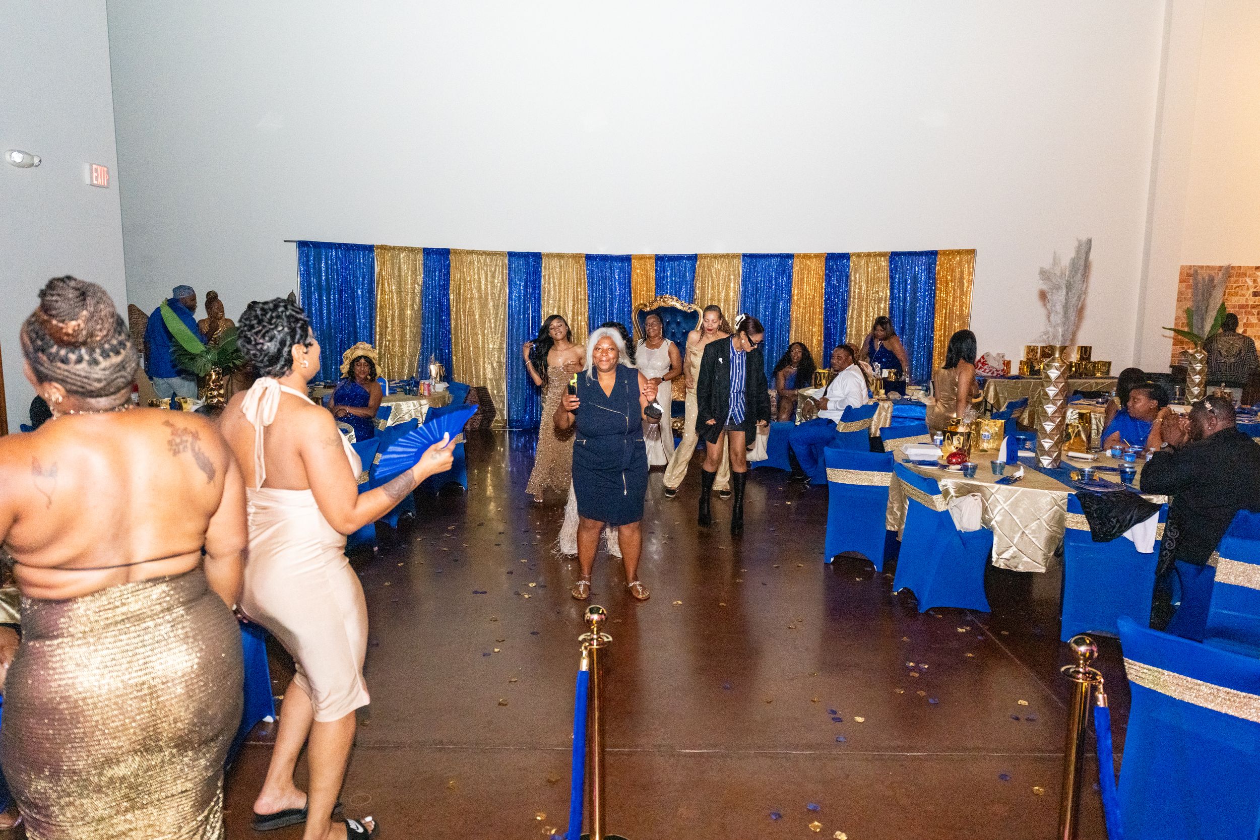 Elegant banquet hall with blue and gold decor, guests in formal attire attending a gala event with draped curtains.