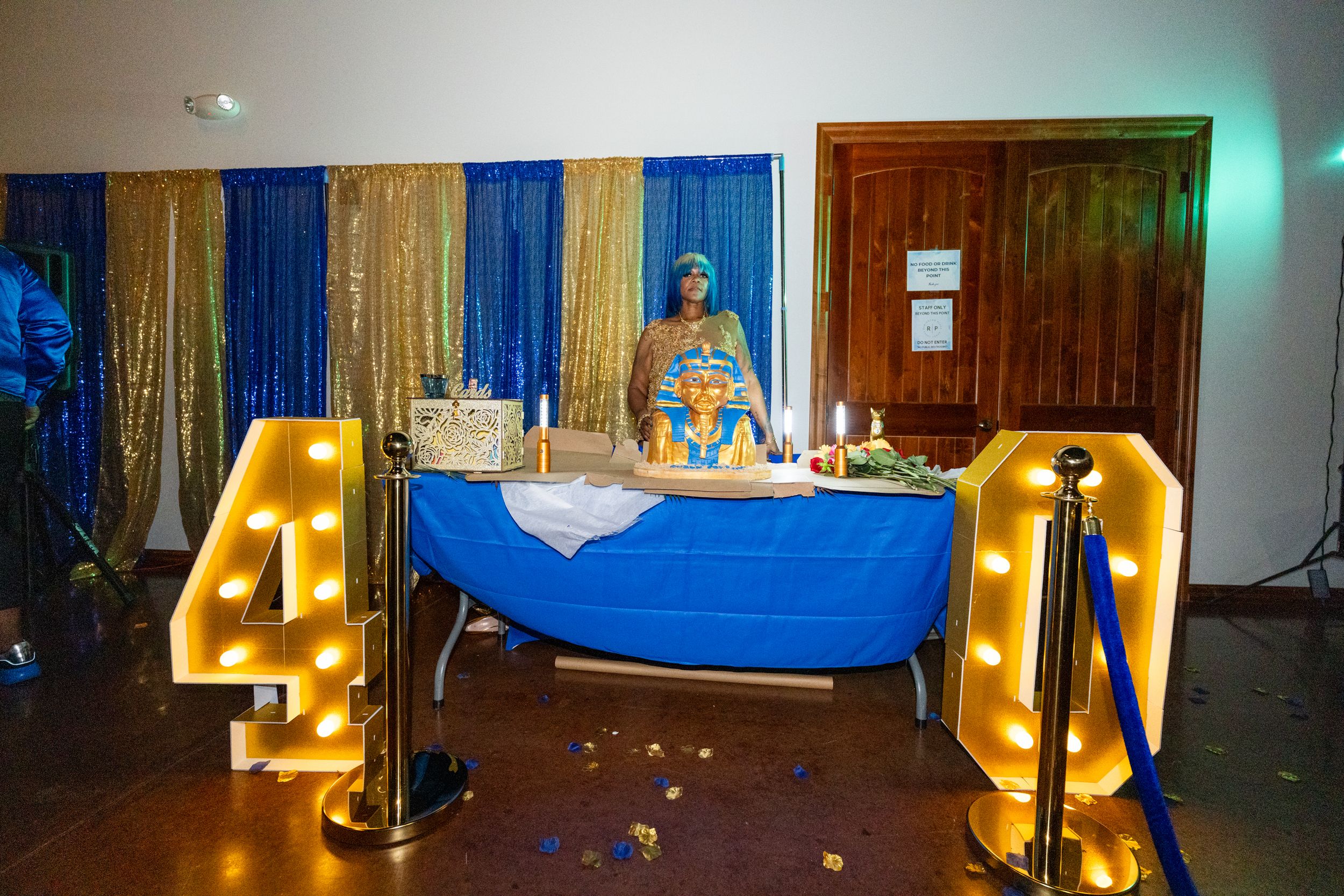 A woman poses at a 40th birthday party table with marquee numbers, blue draping, and gold sequin backdrop.