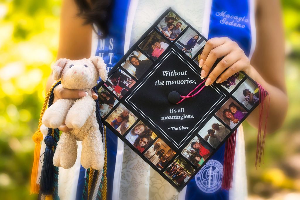 Graduate holds decorated cap with photos and quote 'Without the memories, it's all meaningless' at outdoor ceremony.