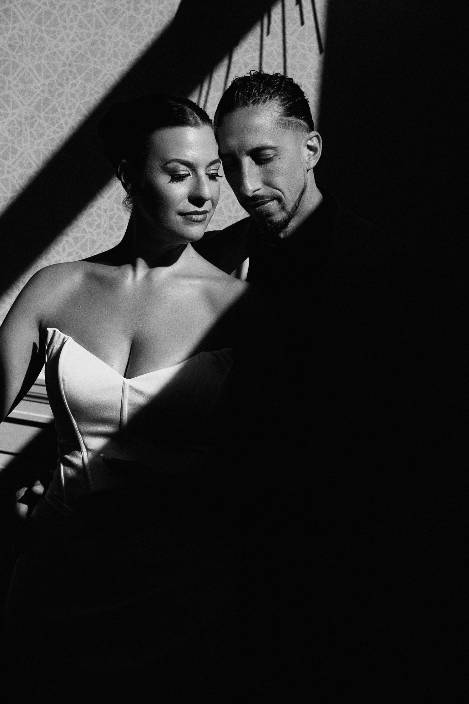 Black and white photo of an elegant couple in dramatic shadow lighting, woman in white dress, man in dark shirt.