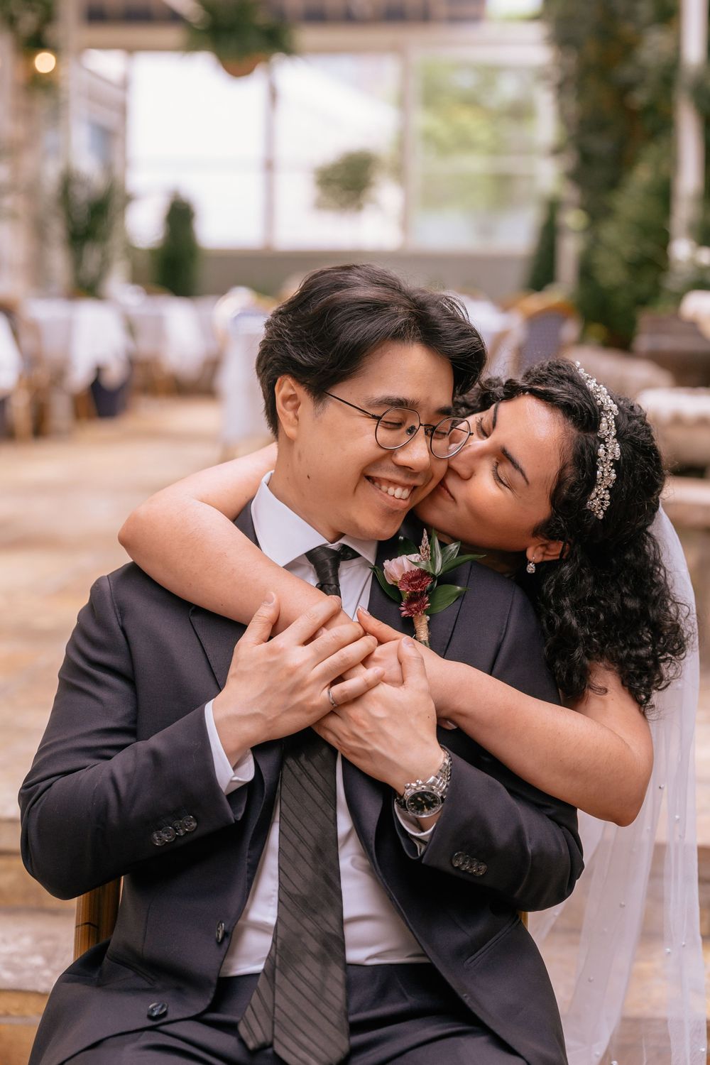 Bride in white veil kisses groom in gray suit on cheek at elegant wedding reception venue.