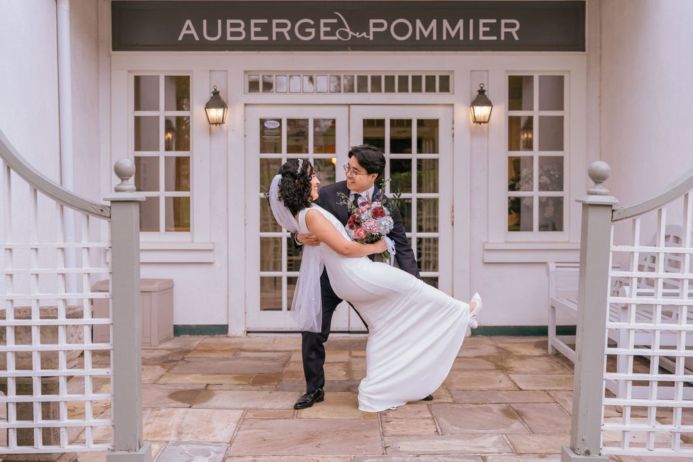 Couple sharing a romantic dip kiss in front of Auberge du Pommier restaurant entrance on their wedding day.