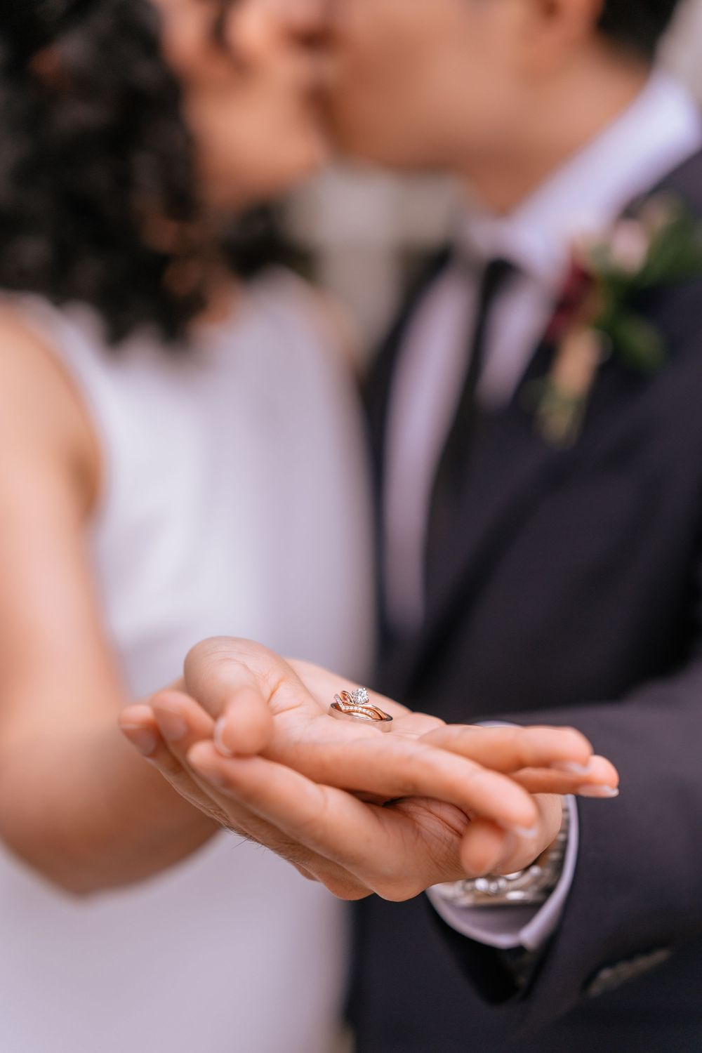 Newlyweds kissing while holding wedding rings in their hands at a wedding ceremony.