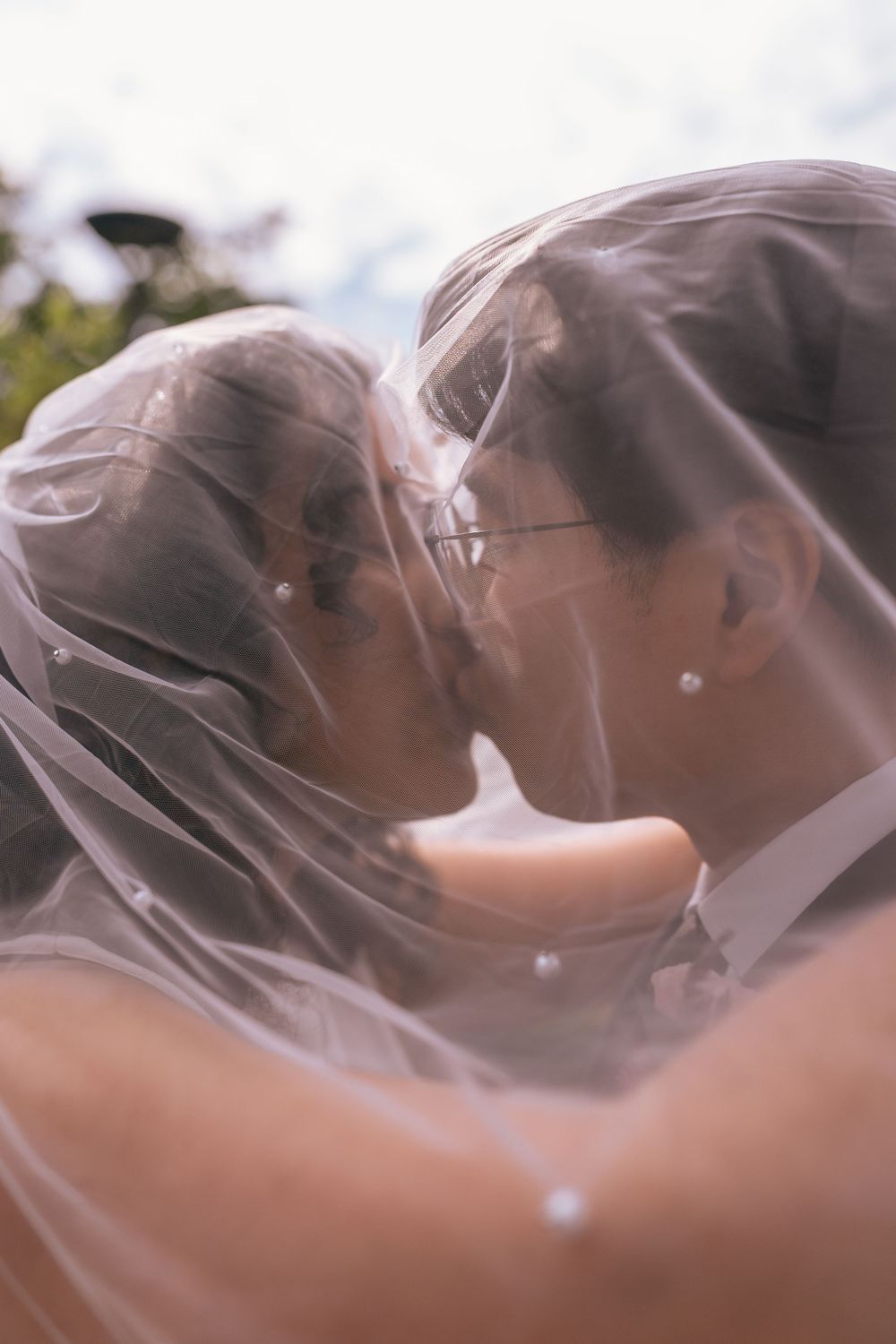 Bride and groom sharing a romantic kiss under a sheer wedding veil outdoors.