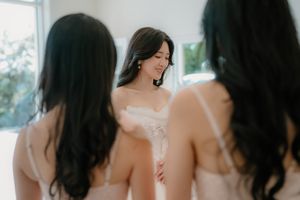 Bride in white strapless gown surrounded by bridesmaids in blush dresses during wedding preparations.