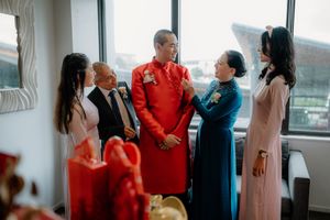 Vietnamese wedding ceremony with family in traditional ao dai attire, groom in red, gathered indoors for a joyful celebration.