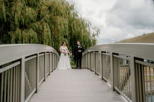 Bride and groom standing together on a scenic bridge with a weeping willow tree backdrop on their wedding day.