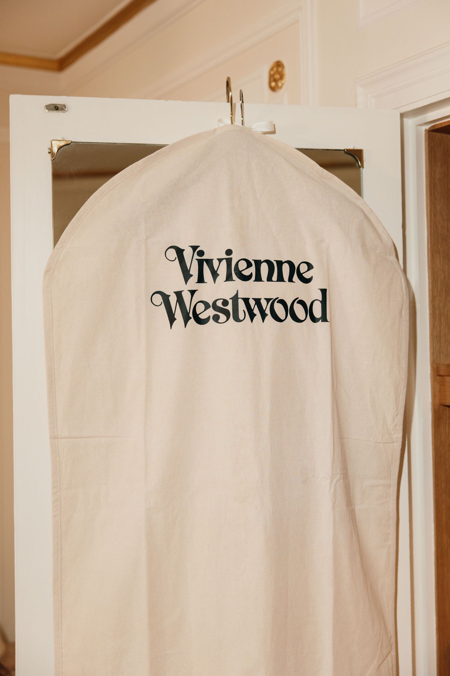Vivienne Westwood garment bag hanging on door hook in bridal preparation room.