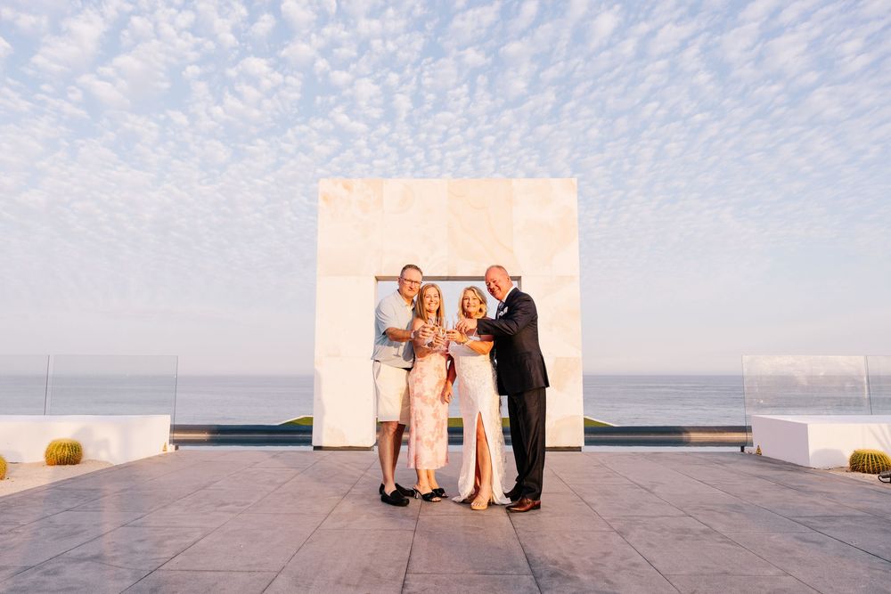 Four people pose together on a rooftop terrace with ocean views and a white stone backdrop at golden hour.