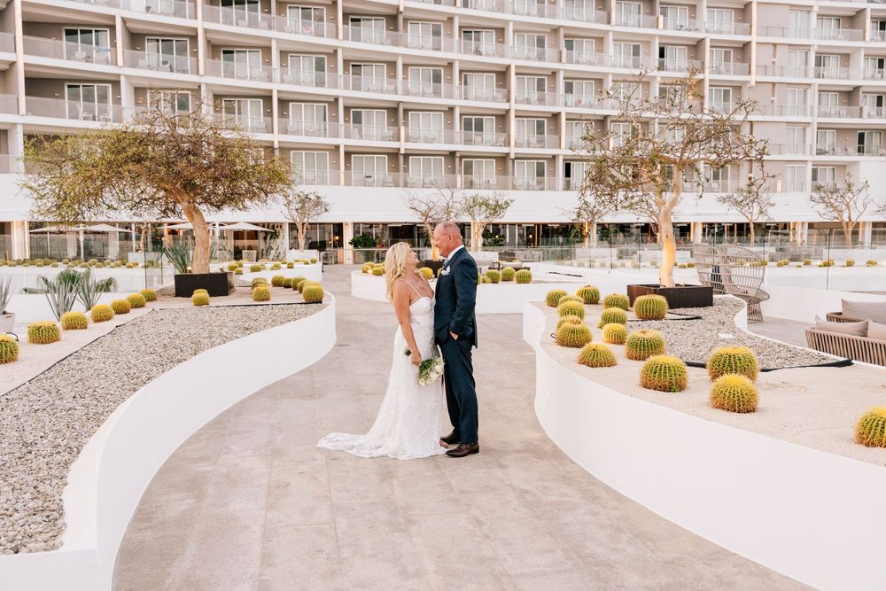 Bride and groom share a romantic moment in a modern hotel courtyard with cacti and manicured gardens.
