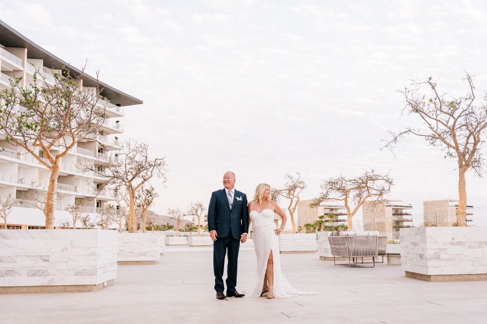 Bride and groom posing outdoors at a luxury resort wedding venue with modern architecture and bare trees.
