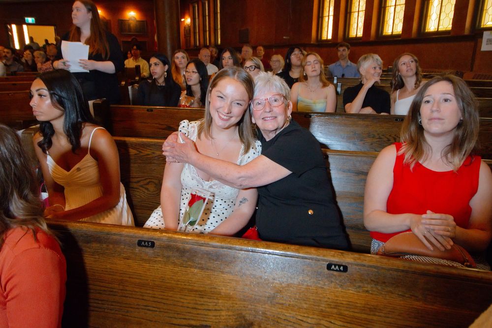 Young girl hugging elderly woman in church pew during a formal ceremony with guests seated in wooden benches.