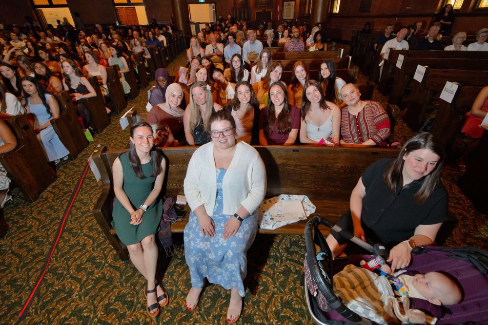 Group of women seated in church pews smile for a photo during a large indoor gathering event.