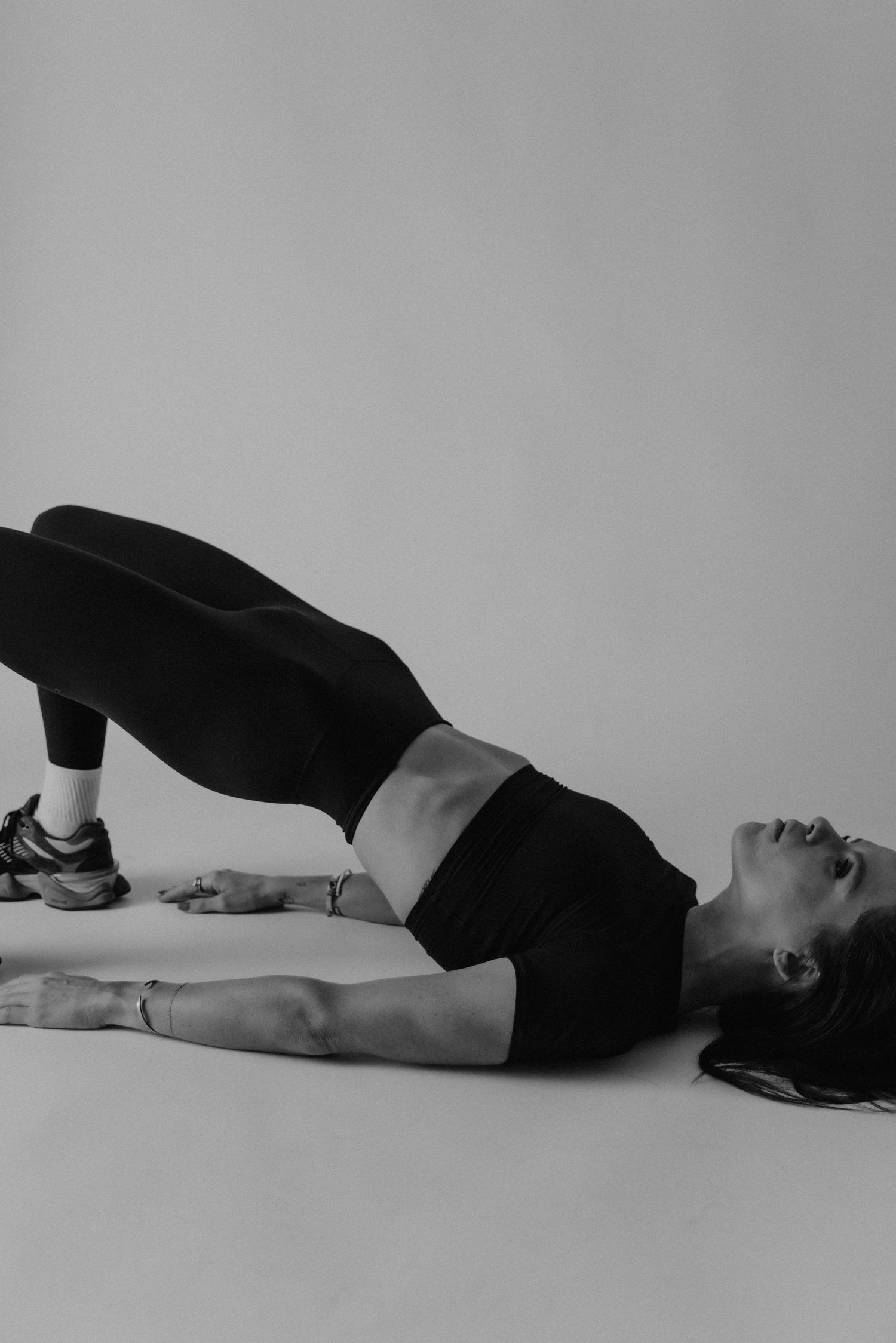 Black and white photo of a woman in athletic wear performing a glute bridge exercise on a studio floor.