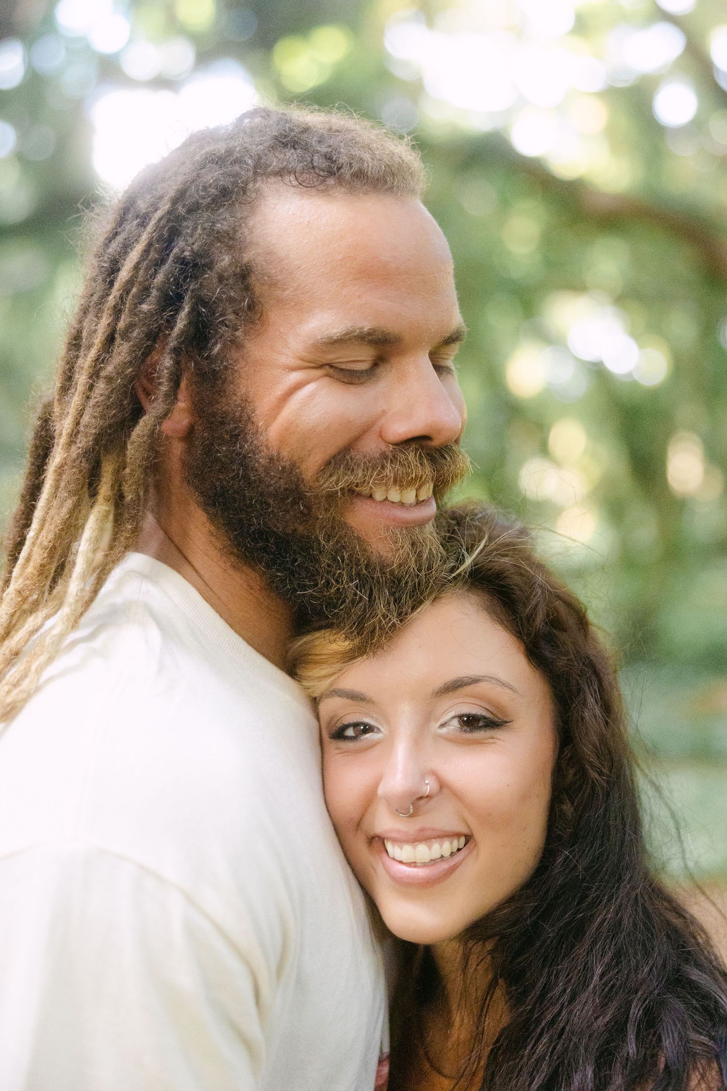 Happy couple embracing outdoors, man with dreadlocks and beard, woman with dark hair smiling.