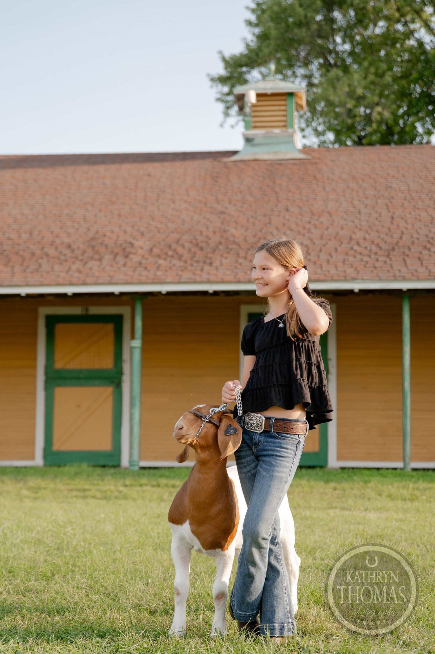 A young girl kneels to nuzzle a white and brown goat at the York Fair, surrounded by colorful fair attractions.