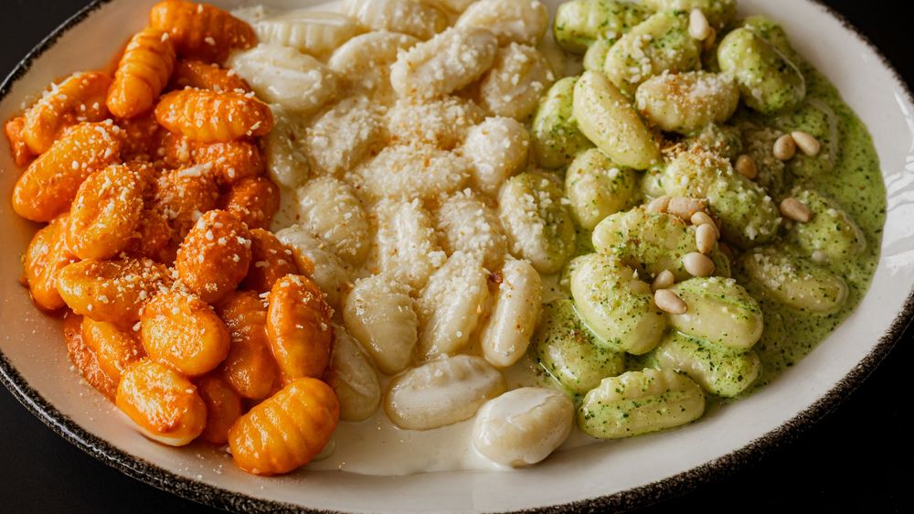 Three varieties of gnocchi on a white plate: tomato, plain, and pesto with pine nuts.