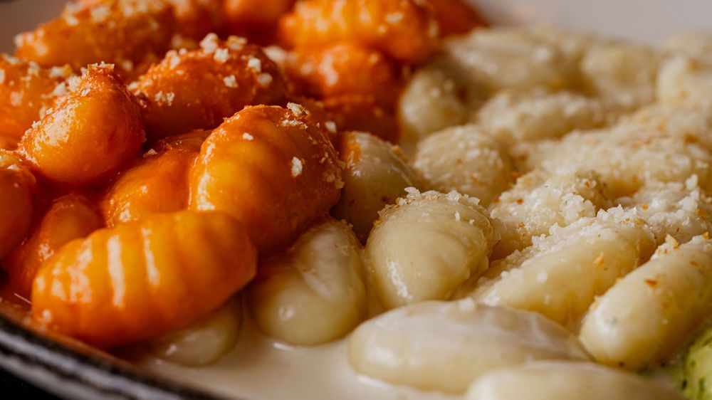 Two-toned gnocchi dish with tomato sauce and butter sauce, topped with breadcrumbs on a white plate.