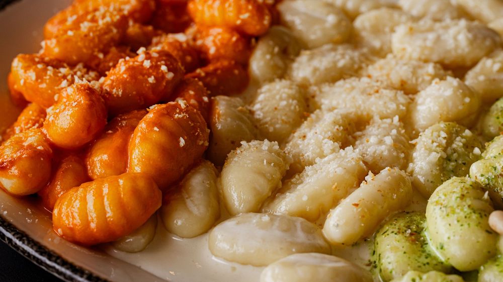 Three varieties of gnocchi on a plate: tomato sauce, butter parmesan, and pesto, garnished with grated cheese.