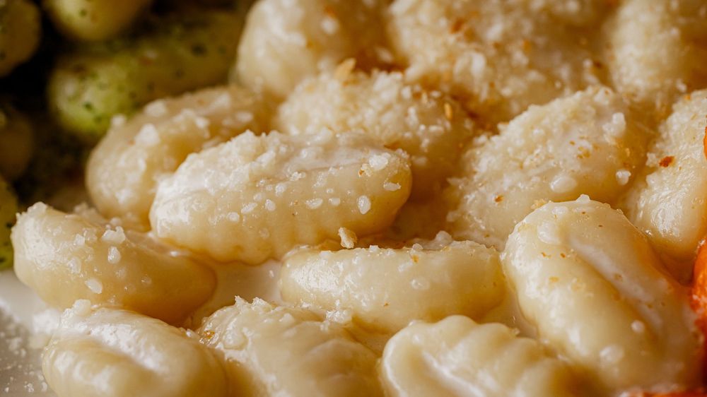 Close-up of homemade gnocchi topped with grated Parmesan cheese on a plate.
