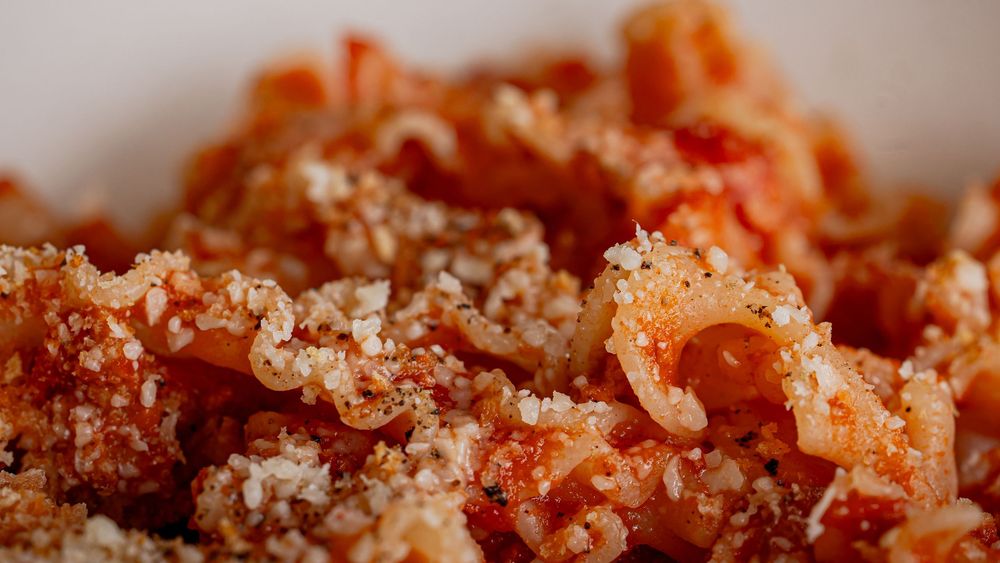 Close-up of pasta in tomato sauce topped with breadcrumbs in a white bowl.