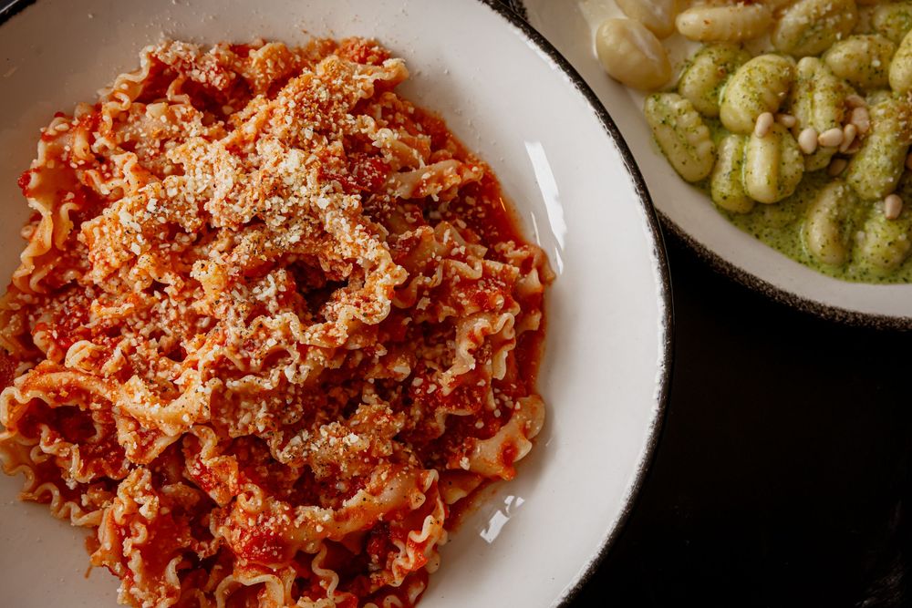 Plate of lasagne pasta with rich tomato sauce and Parmesan cheese beside a dish of green gnocchi.
