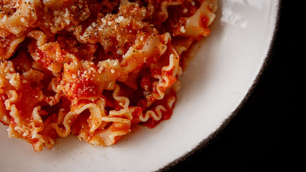 A white plate of ruffled lasagna pasta in rich tomato meat sauce, topped with grated Parmesan cheese.