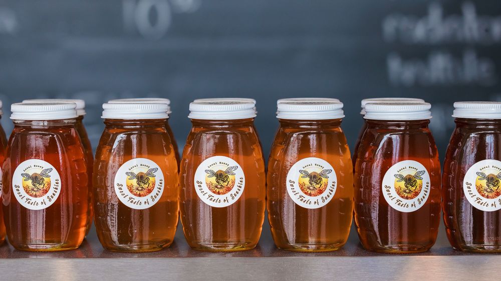 Row of honey jars with branded labels displayed on a shelf in a store.