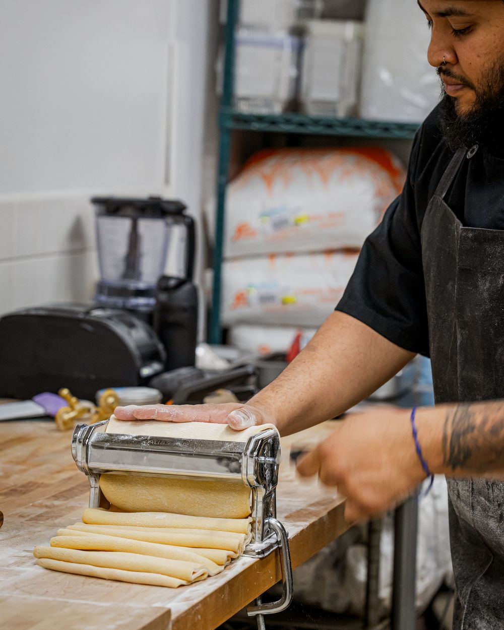 Chef using a pasta machine to roll fresh homemade pasta dough in a professional kitchen.