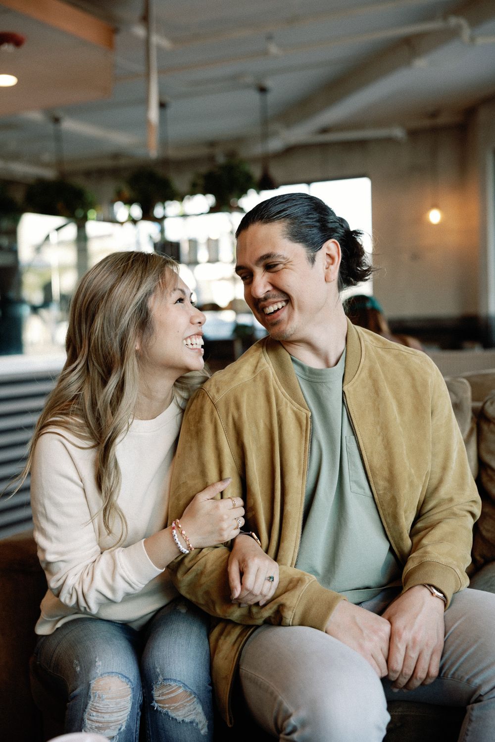 Happy couple smiling at each other while sitting together in a cozy cafe, wearing casual outfits.