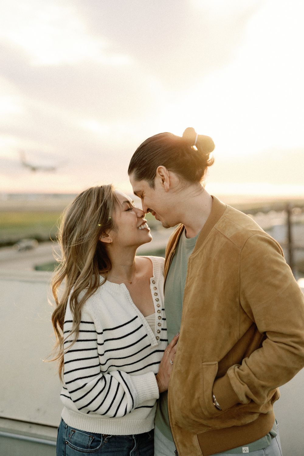 Romantic couple sharing an intimate moment at sunset, woman in striped sweater and man in brown jacket touching foreheads.