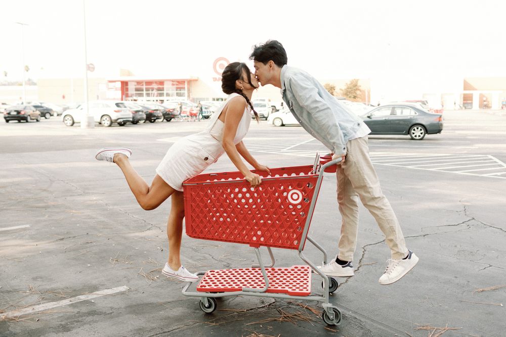 Couple sharing a kiss in a red Target shopping cart in a parking lot outside a Target store.