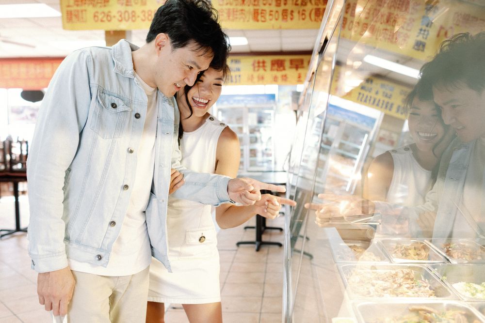 Happy Asian couple smiling and browsing food display case at a Chinese restaurant or market.