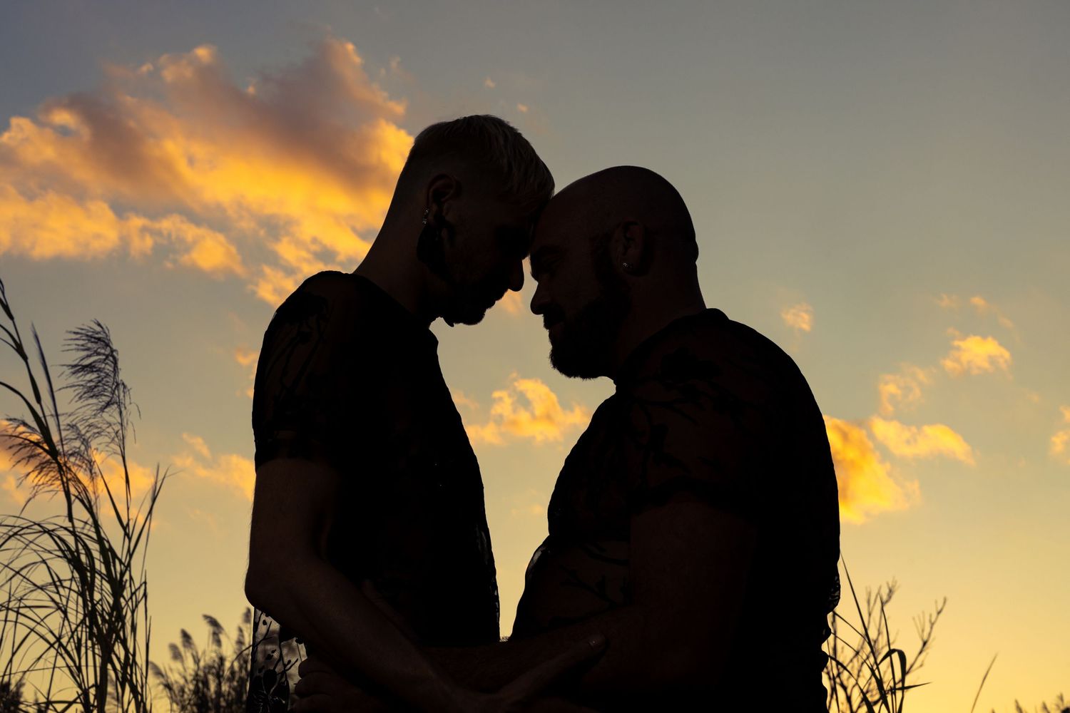 Silhouette of two men facing each other at sunset with dramatic orange clouds in the background.