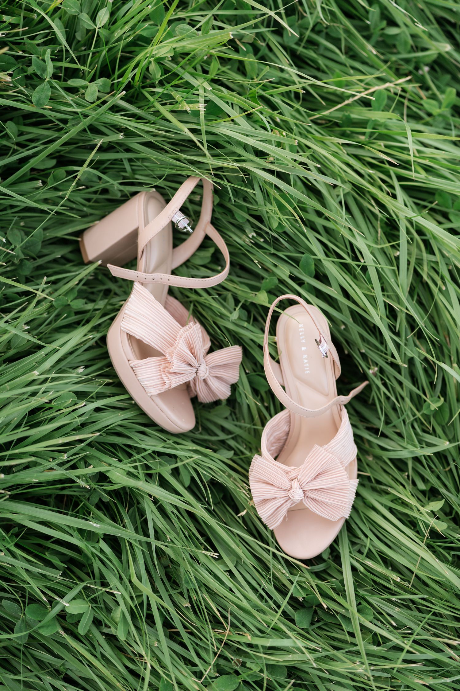 Pink block heel sandals with bow detail resting on lush green grass, perfect for outdoor weddings.