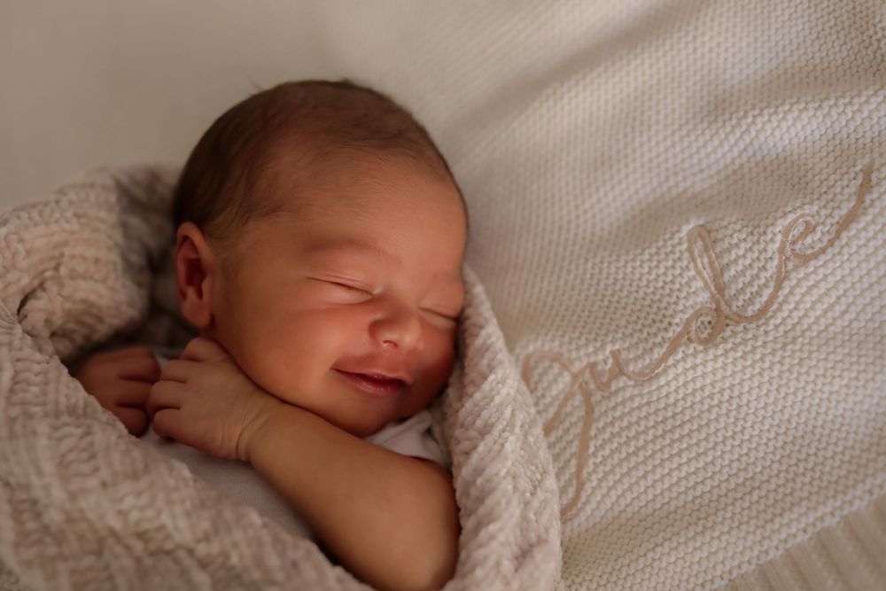 Peaceful newborn baby sleeping wrapped in a soft cream knit blanket with embroidered details.