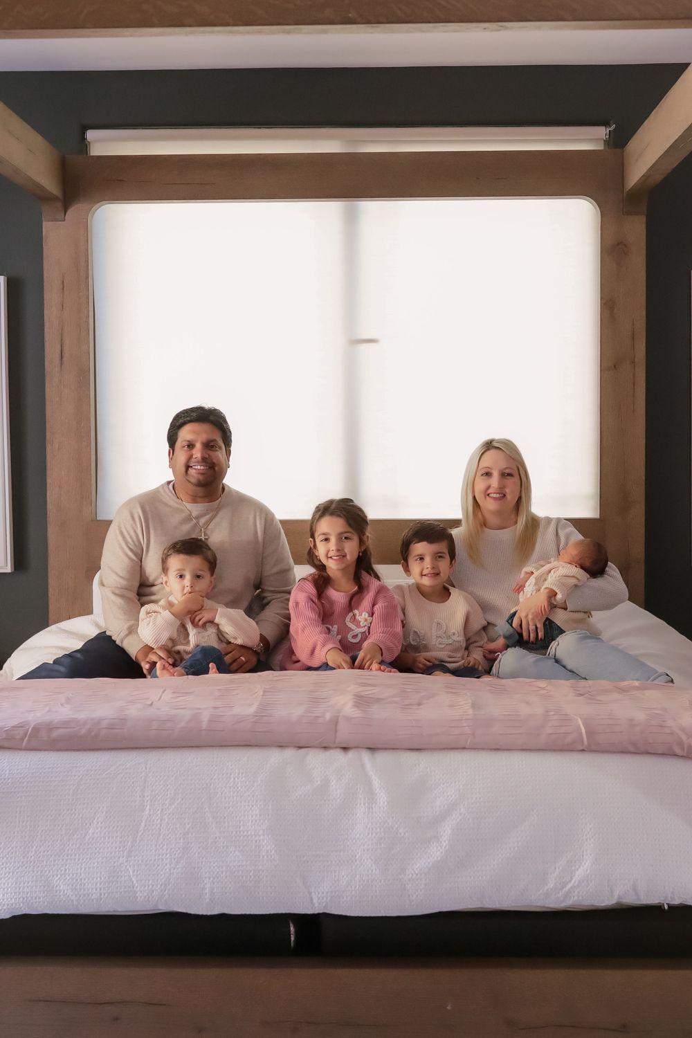 Happy family of six posing together on a large canopy bed in a modern bedroom.