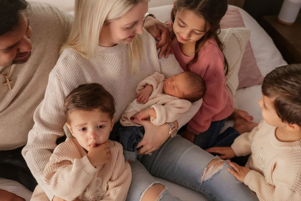 Parents and four children gather closely together on a bed, lovingly admiring their newborn baby.